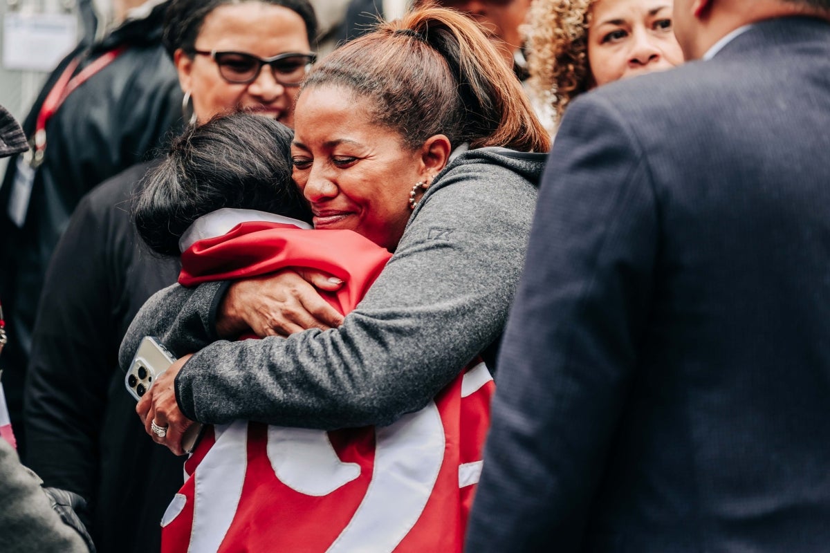 Two alums embrace in a huge one wearing the class banner