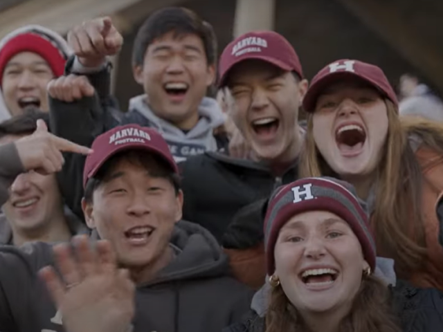 Harvard students smile and wave to the camera at the Harvard-Yale Game.
