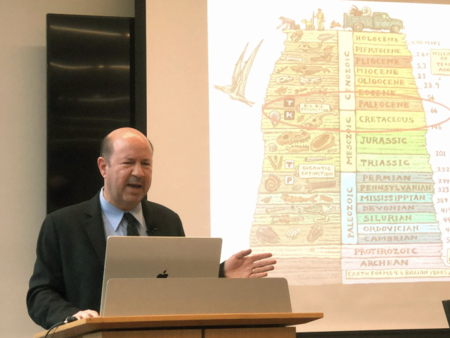 Michael Mann at podium in front of a diagram of the geologic time scale