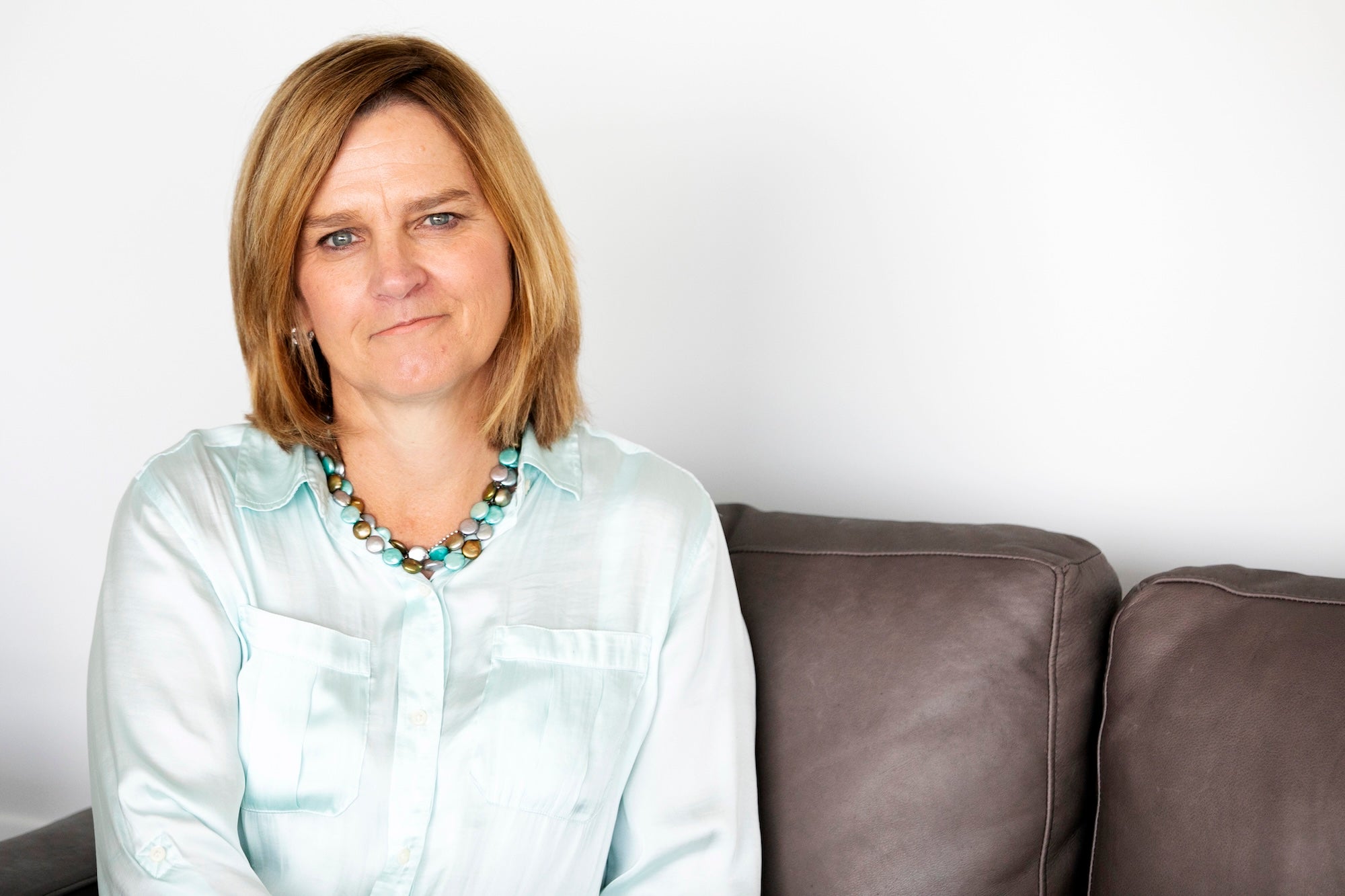 Karen wearing an aqua colored shirt, sitting on a brown leather couch