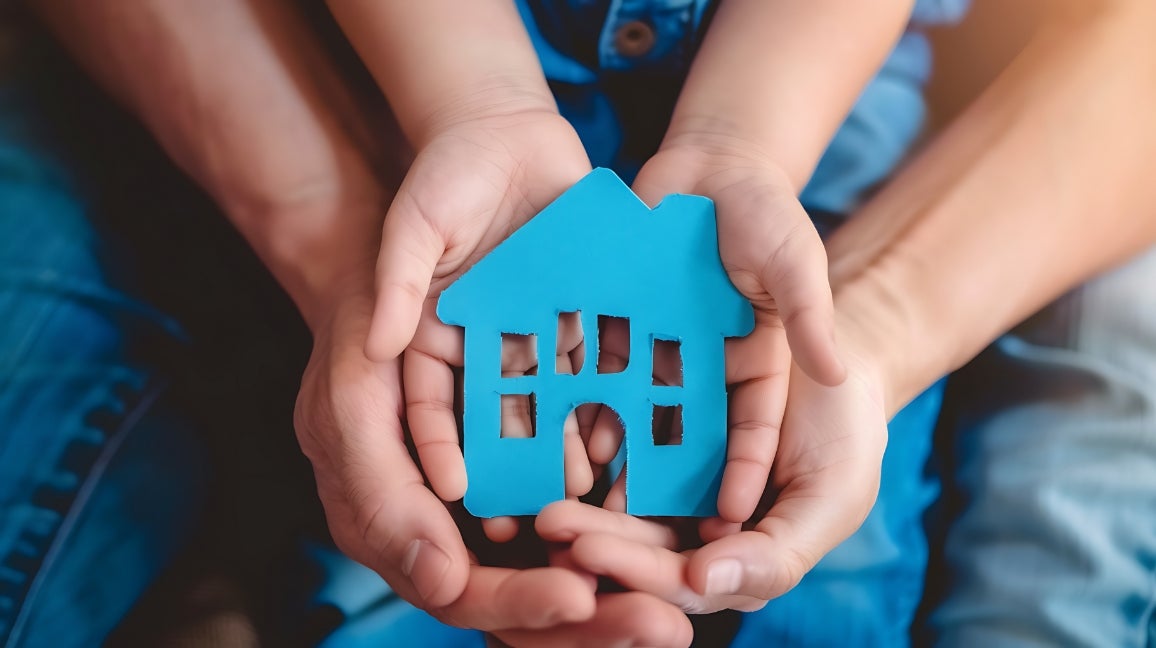 Close-up of adult and child hands holding a blue clay cut-out of a house.