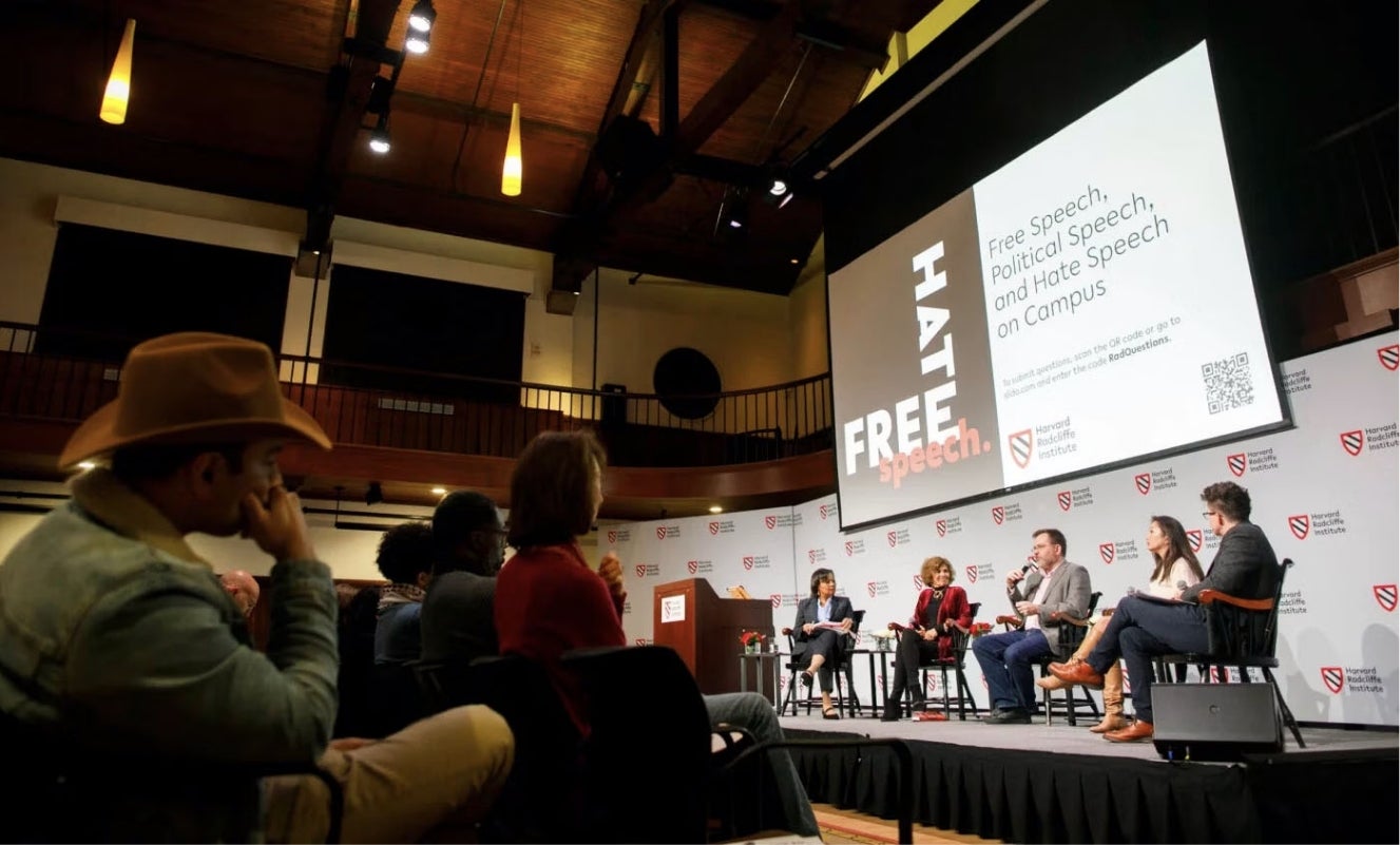 Five panelists sit on stage at a Harvard Radcliffe Institute event with audience members seated in the foreground