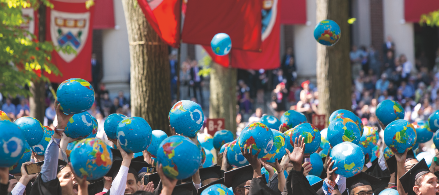 Harvard graduates hold miniature globes above their heads during Commencement in Tercentenary Theatre.