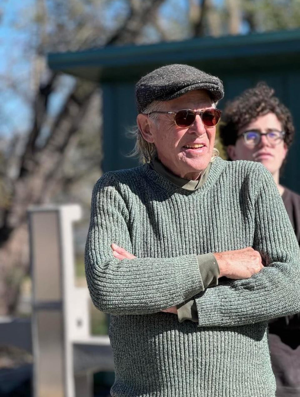 Bill McBride stands with his arms crossed and sunglasses with a person directly behind him.
