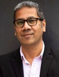 Tan man with glasses and hair turning grey wearing a suit