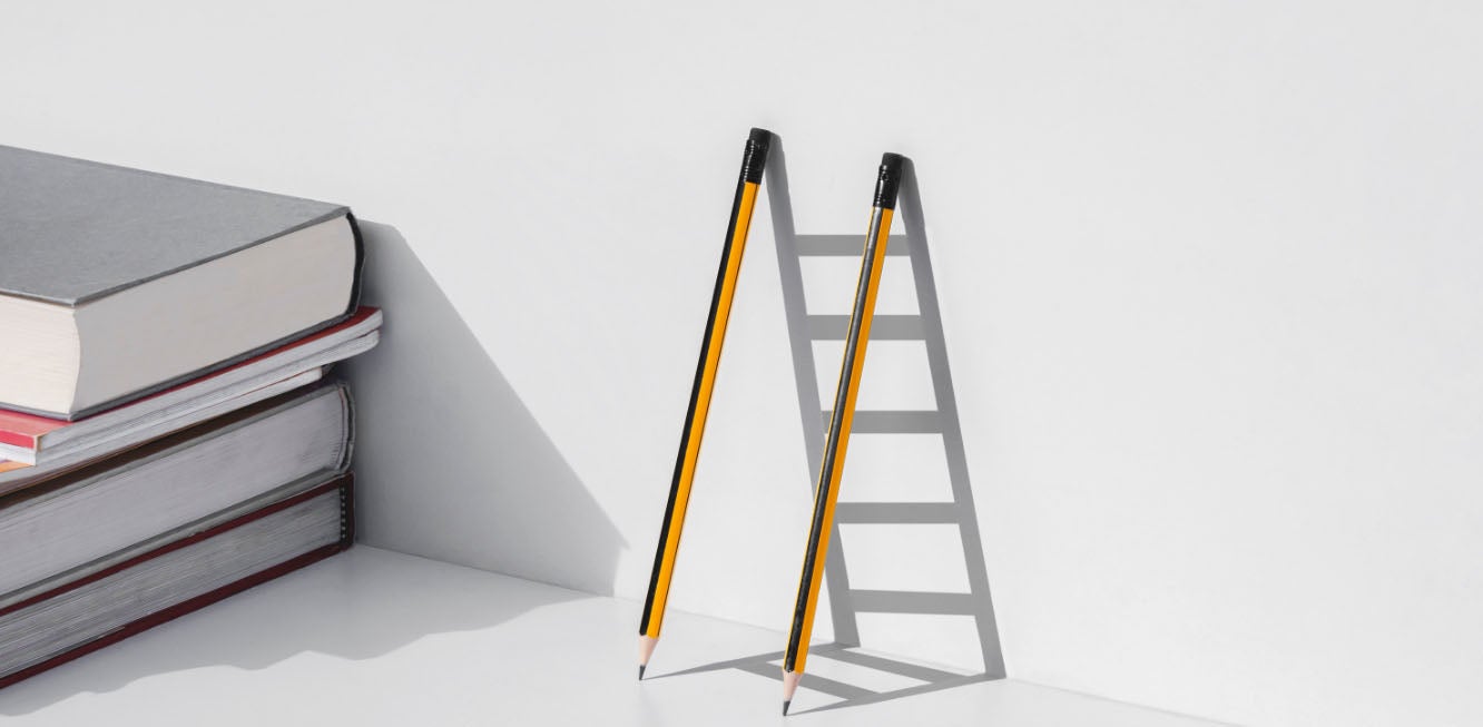 Two pencils leaning on a wall leaving the shadow of a ladder