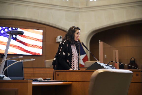 Ana Sandoval stands at podium with American flag graphic behind her. 