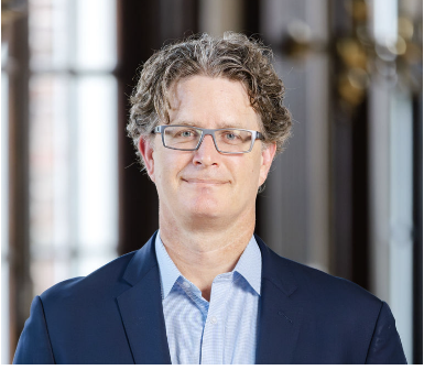 headshot of white man, mid-40s with curly grey hair, blue eyes and glasses