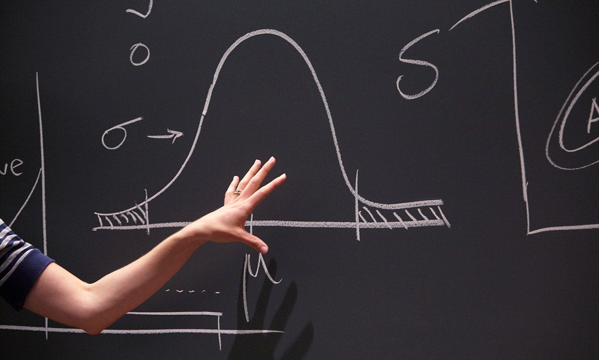 A biostatistics student gestures toward a blackboard with a bell curve