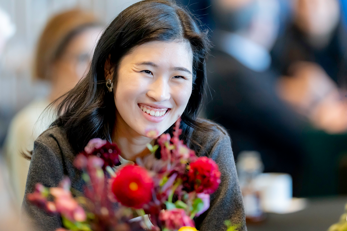 A woman smiling in front of a red floral centerpiece.