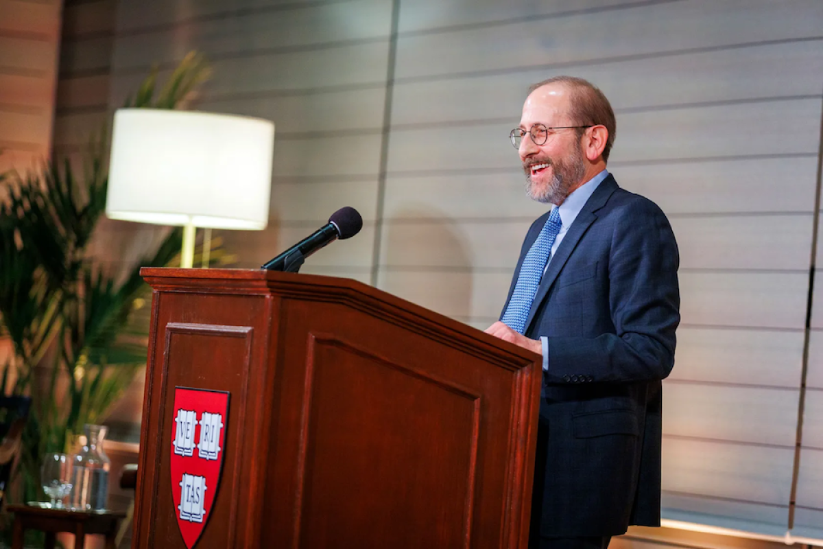 Alan Garber stands behind a wooden dais adorned with the Harvard shield