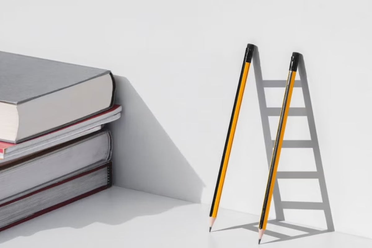 A stack of books next to two pencils leaning on a wall leaving the shadow of a ladder