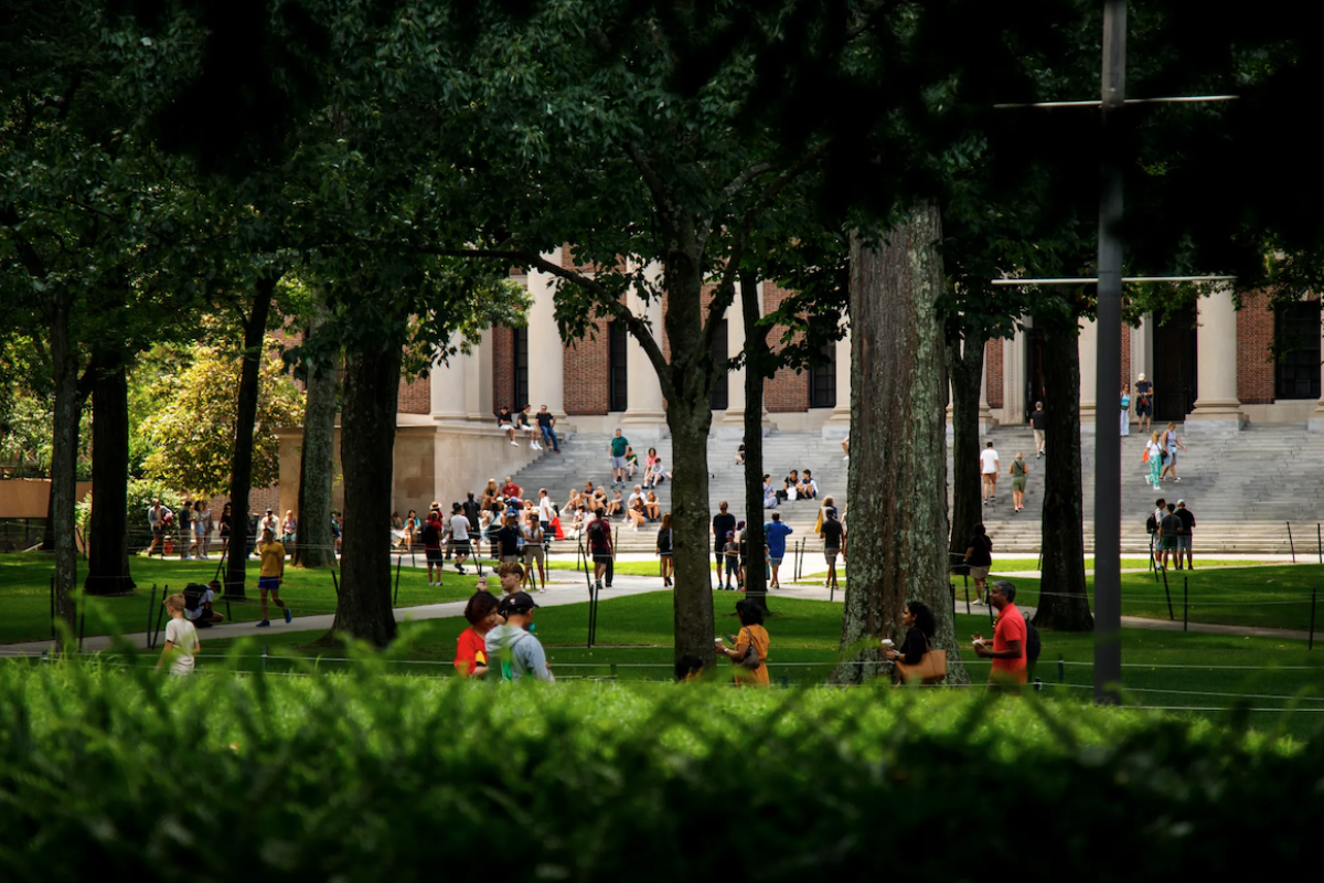 Greenery in the forground with students walking on campus and Widener Library in the background