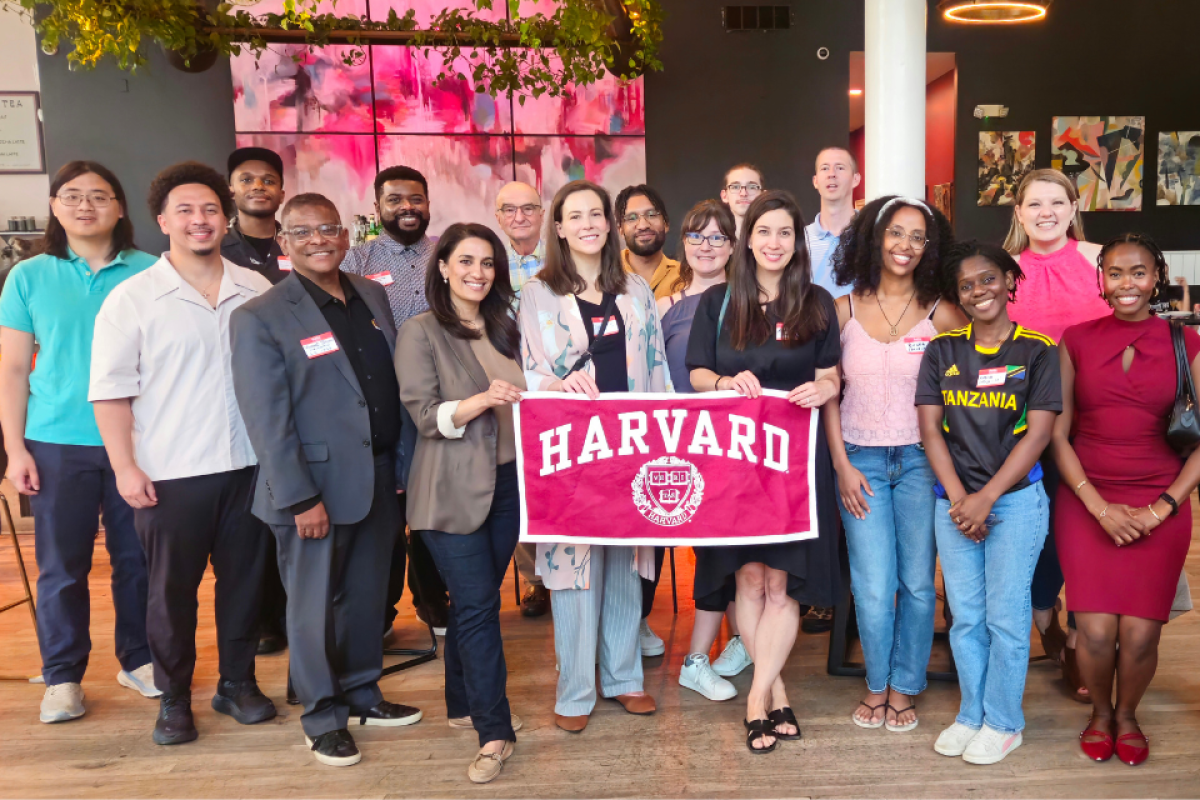 Group of people posing indoors while holding a Harvard banner