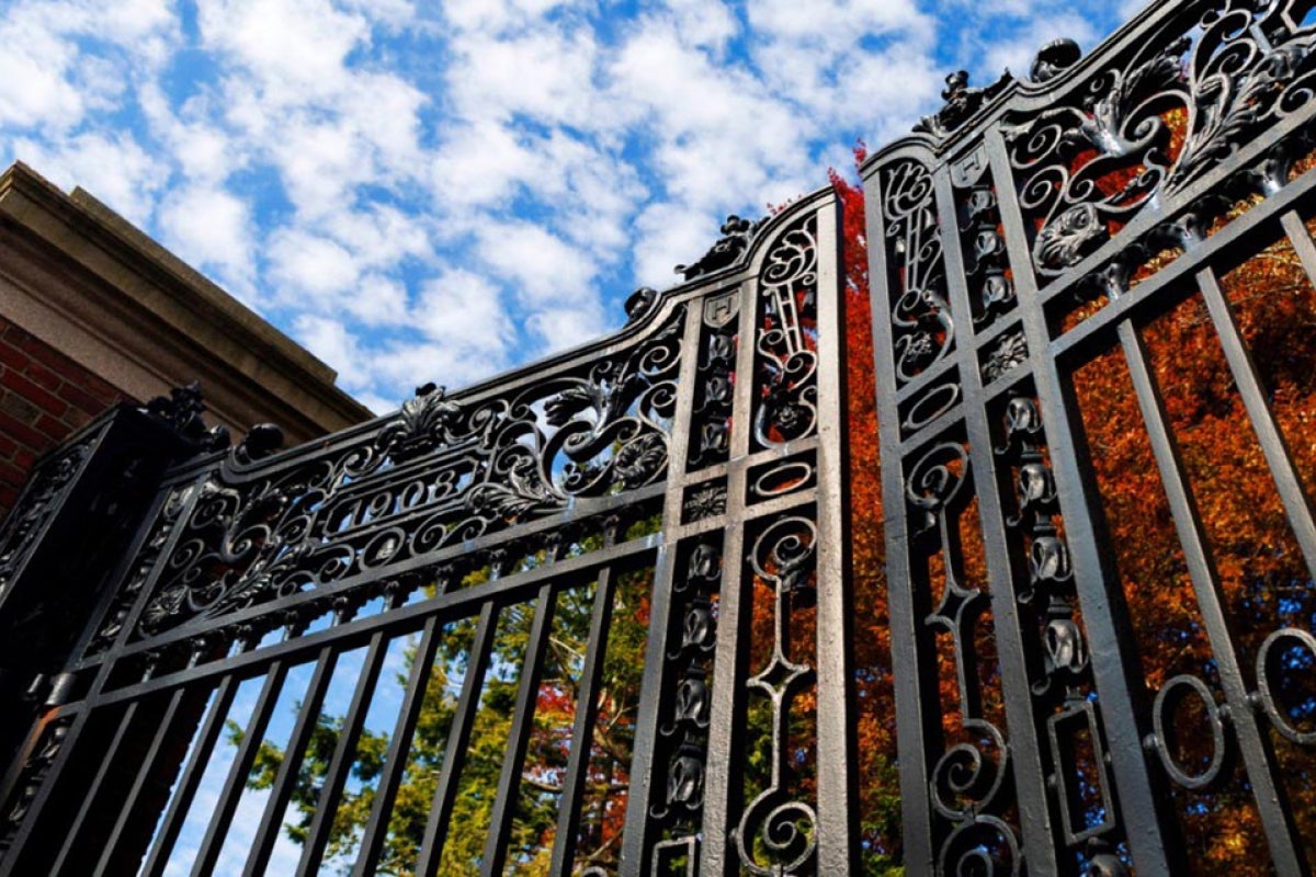 Harvard Gate and column with blue sky and white clouds above and red fall foliage in the background