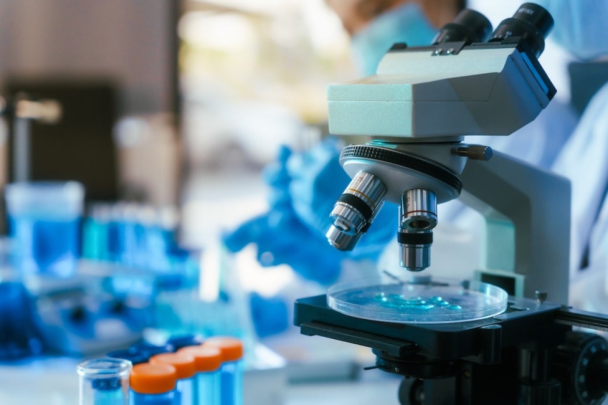 A microscope in a laboratory, with test tubes of blue liquid in the foreground