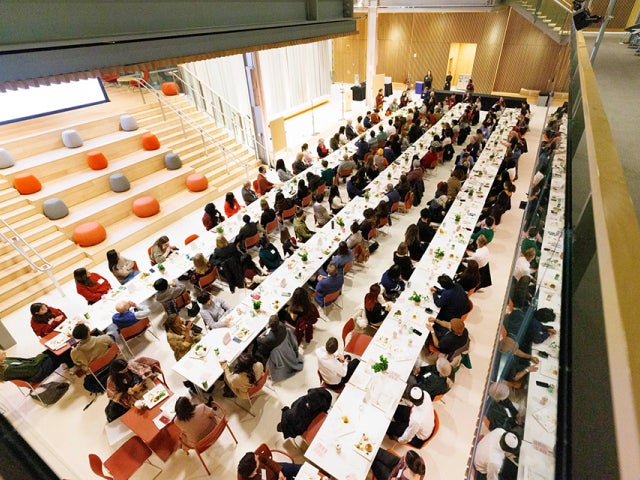 A large group gathers for a long-table interfaith dinner in the campus center, viewed from above.