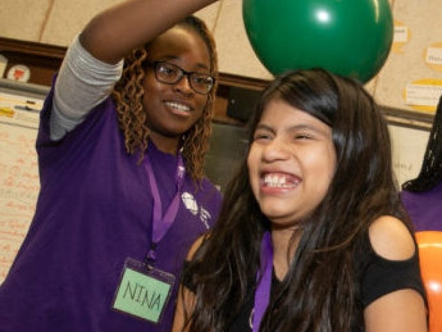 Harvard College student Nina Uzoigwe demonstrates static electricity with a balloon on the head of an Amigos School student