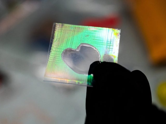 A hand wearing a black glove holds two small planes of glass with an iridescent greenish material between. Part of the space between the panes has become transparent.