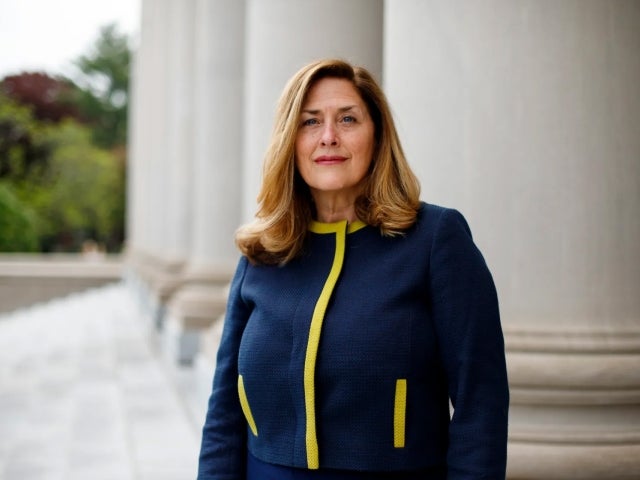 Suzanne Glassburn stands in front of columns in navy and yellow sweater