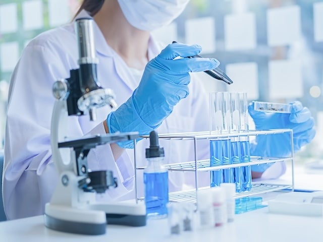  Scientist handling test tubes filled with blue liquid beside a microscope and other laboratory equipment