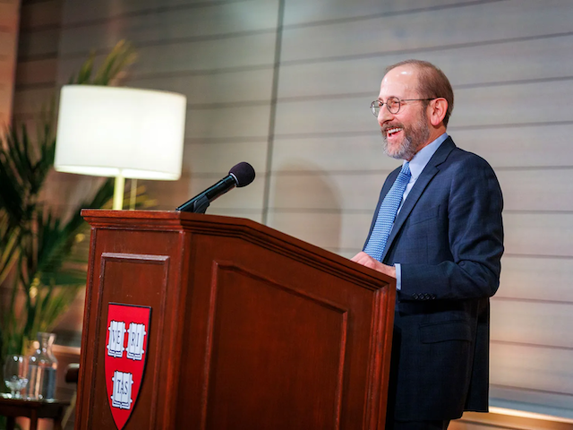 Alan Garber stands behind a wooden dais adorned with the Harvard shield