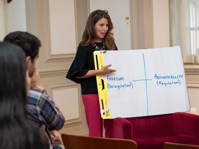 A woman points to a chart on a large pad of paper that shows "freedom" on one access and "accountability" on the other; two other people listen in the foreground