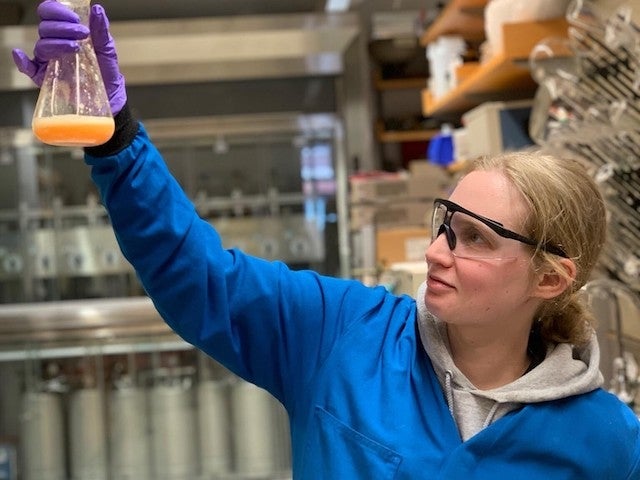 Emily Kerr holds up a beaker containing an orange liquid