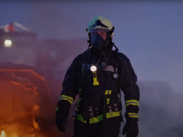 A firefighter in protective gear with flames and smoke in the background