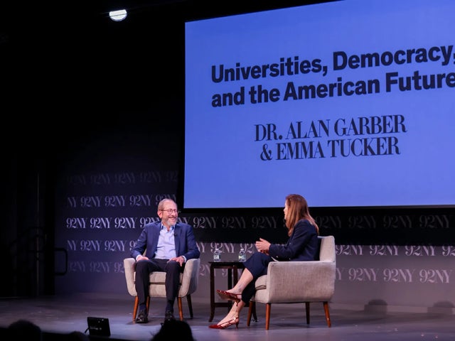 President Garber and Emma Tucker sit on stage with Universities, Democracy, and the American Future sign behind them.