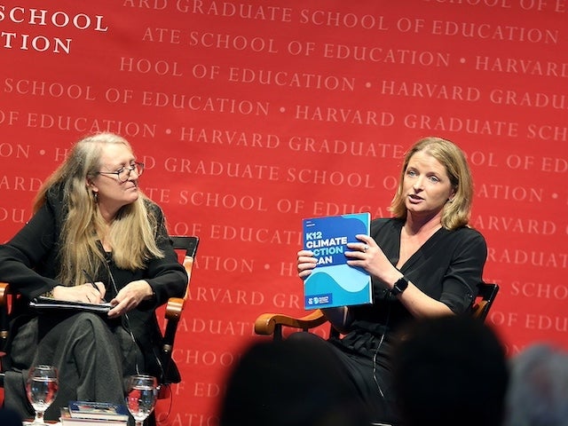 Laura Schifter holds up a report titled "K12 Climate Action Plan" from the stage at a Harvard Graduate School of Education event