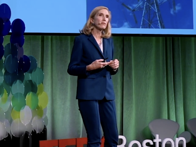 Kari Nadeau standing on a stage in front of the TEDx Boston logo and a green curtain