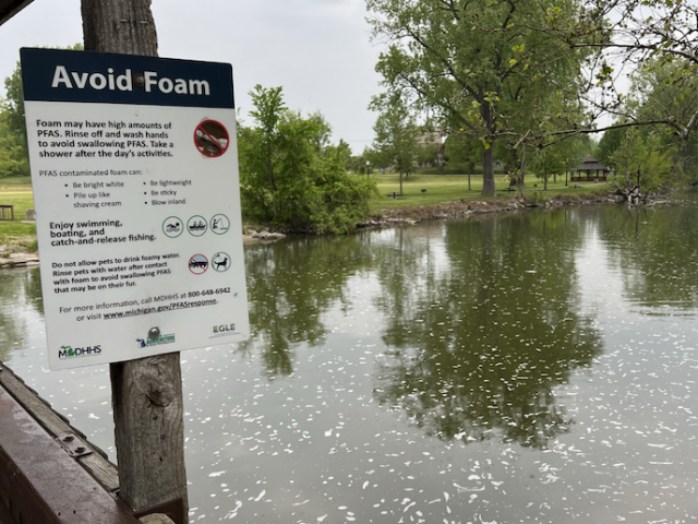 Photo of a lake with a sign that says "Avoid Foam," as it may have high amounts of PFAS.