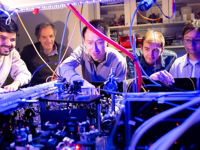 Five people examine an array of complex laboratory equipment with colorful wires and lights