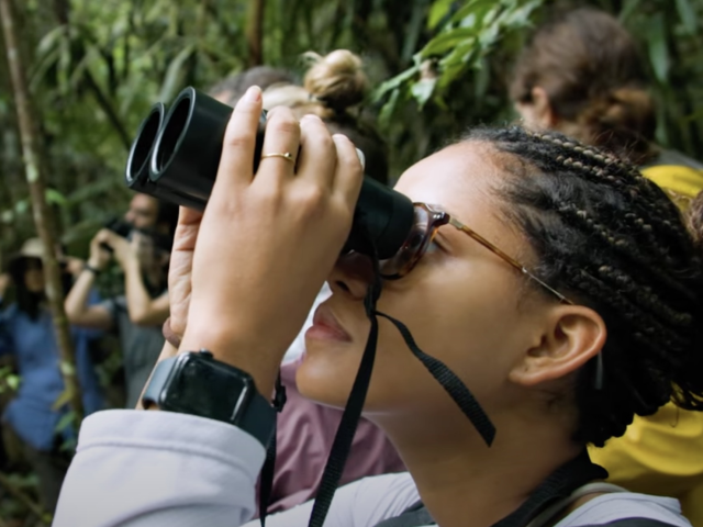 A participant of the Harvard Amazon Rainforest Immersion looks through binoculars 