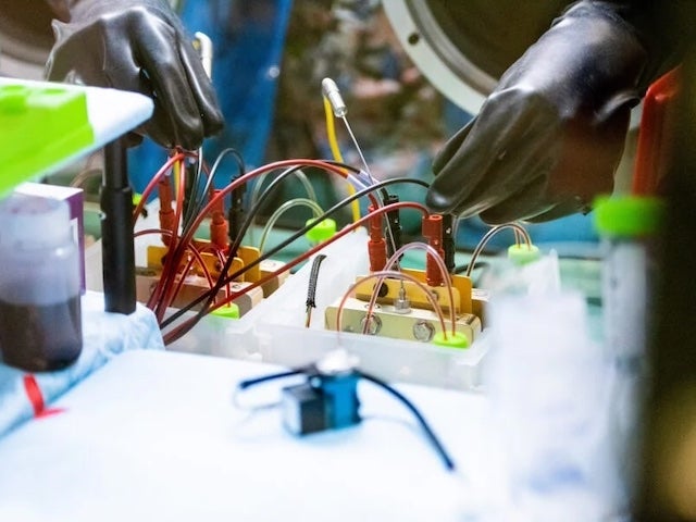 Close up of gloved hands working on a device with red and black wires coming out of it
