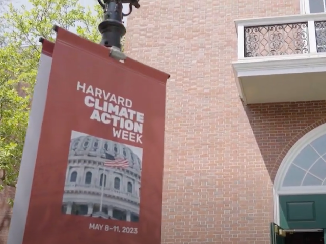 A banner for Harvard Climate Action Week hands on a lamppost in front of a brick building