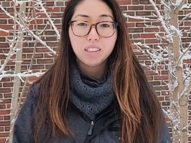 Student stands in a snowy landscape with a brick wall behind her