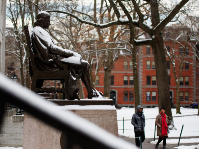 John Harvard statue covered in snow with two people walking by