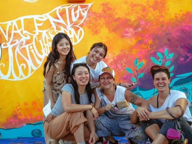 Five women in front of a brightly colored mural