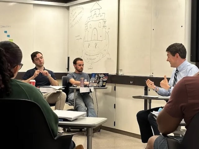 People sitting in a classroom having a discussion in front of a whiteboard.
