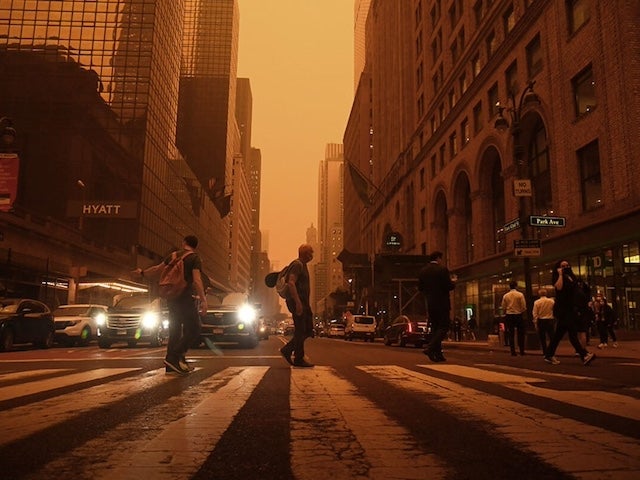 People crossing a busy street in New York City under a hazy sky tinted orange from wildlife smoke
