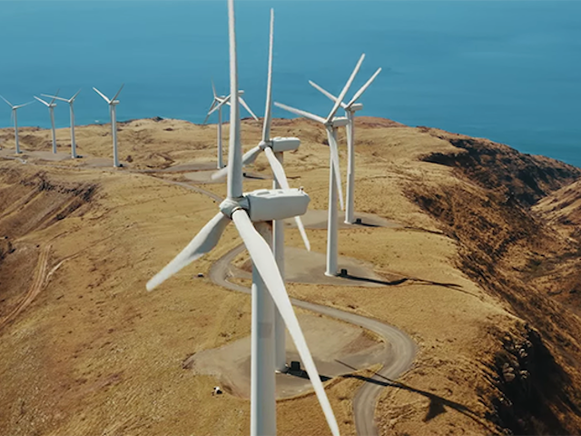 An array of wind turbines line a hill near a body of water