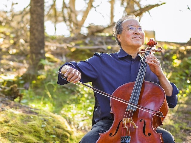 Yo-Yo Ma seated and smiling, playing cello among trees and sunshine