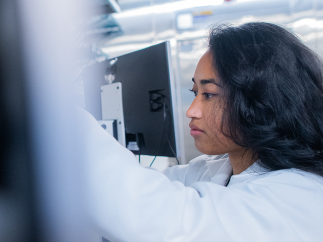 A researcher in a white lab coat works with scientific equipment in a laboratory setting. 