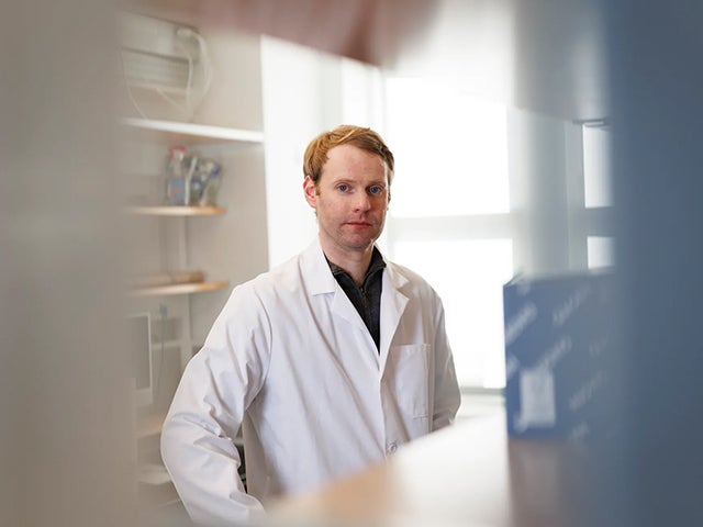 Andrew Kruse wears white lab coat in lab