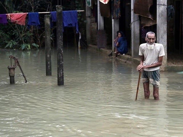 A man with a cane stands in knee-high floodwaters in Bangladesh