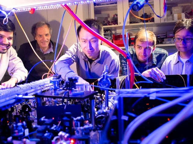 Researchers work together around a complex lab experiment with wires and optical equipment.