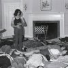 A black-and-white archival photograph shows a woman standing in the center of a room while a group of people lie on the floor around her, suggesting a guided workshop or consciousness-raising session.