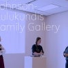 Three people stand in conversation around a pedestal in a minimalist gallery space.